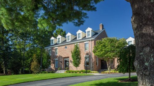 Lincoln Brick Colonial exterior with dormer windows, manicured lawn, and mature trees